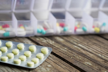 Variety of pills in white plastic pill organizer on weathered wood