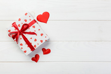 Valentine or other holiday handmade present in paper with red hearts and gifts box in holiday wrapper. Present box gift on white wooden table top view with copy space, empty space for design