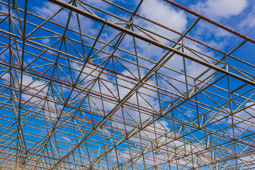 Urban abstract texture background. Point of view looking up in blue sky through old rusty geometric diagonal metal constructions of abandoned building. Horizontal color photography.