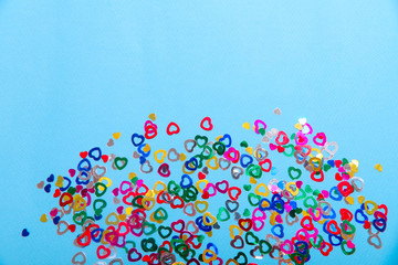 Many small colored hearts at the bottom of a blue background. Valentine's day concept. Horizontal, space for text, top view, abstract background.