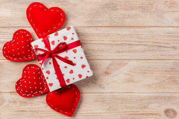 Valentine or other holiday handmade present in paper with red hearts and gifts box in holiday wrapper. Present box of gift on orange wooden table top view with copy space, empty space for design