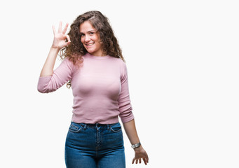 Beautiful brunette curly hair young girl wearing pink sweater over isolated background smiling positive doing ok sign with hand and fingers. Successful expression.