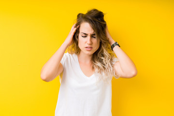 Young beautiful blonde woman over yellow background with hand on head for pain in head because stress. Suffering migraine.