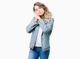 Beautiful young blonde woman wearing denim jacket over isolated background sleeping tired dreaming and posing with hands together while smiling with closed eyes.