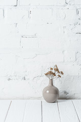 bouquet of dried flowers in ceramic vase near white brick wall