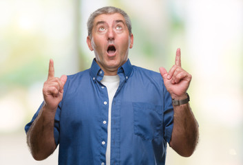 Handsome senior man over isolated background amazed and surprised looking up and pointing with fingers and raised arms.