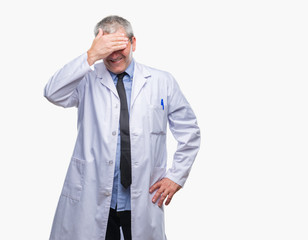 Handsome senior doctor, scientist professional man wearing white coat over isolated background smiling and laughing with hand on face covering eyes for surprise. Blind concept.