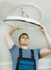 Male electrician mounting LED lamp at home.