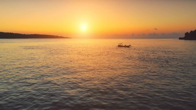 Drone Flight over Sunset Ocean. Boats sailing in soft orange light. Travel Vacation Recreation Paradise Tourism. Beautiful nature landscape in Tropical Nusa Penida Bali Island, Indonesia. 4K Zoom out