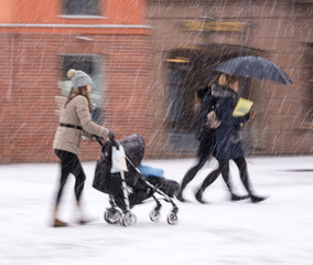 Obraz premium Mother walks with the child in the stroller in snowy winetr day. Intentional motion blur. Defocused image