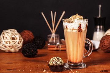 Beautifully decorated latte macchiato coffee with whipped cream and sprinkled with crushed halva, in high transparent glass, on a wooden table, on a dark background