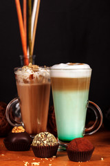Coffee latte macchiato with mint syrup and whipped cream, in high transparent glasses, on a wooden table, on a dark background with cakes