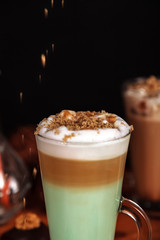 Coffee latte macchiato with mint syrup and whipped cream, sprinkled with chopped halva, in high transparent glasses, on a wooden table close-up, selective focus