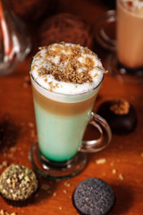 Coffee latte macchiato with mint syrup and whipped cream, sprinkled with chopped halva, in high transparent glasses, on a wooden table