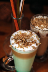 Coffee latte macchiato with mint syrup and whipped cream, sprinkled with chopped halva, in high transparent glasses, on a wooden table