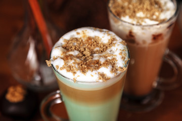 Coffee latte macchiato with mint syrup and whipped cream, sprinkled with chopped halva, in high transparent glasses, on a wooden table close-up, selective focus