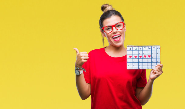 Young beautiful woman holding menstruation calendar over isolated background pointing and showing with thumb up to the side with happy face smiling