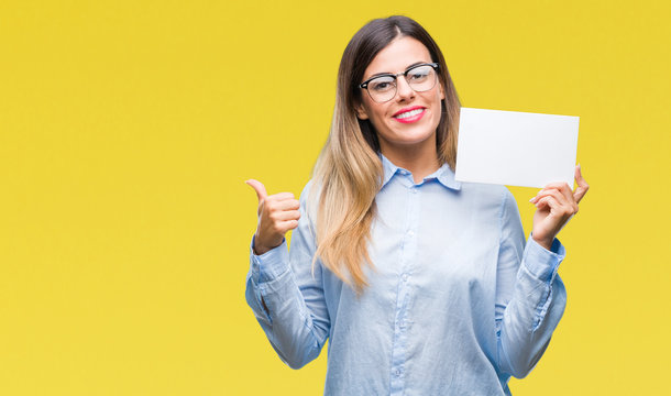 Young beautiful business woman holding blank card over isolated background pointing and showing with thumb up to the side with happy face smiling