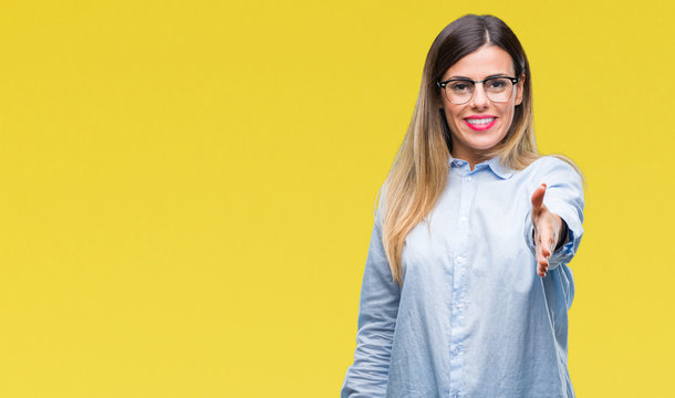 Young beautiful business woman wearing glasses over isolated background smiling friendly offering handshake as greeting and welcoming. Successful business.