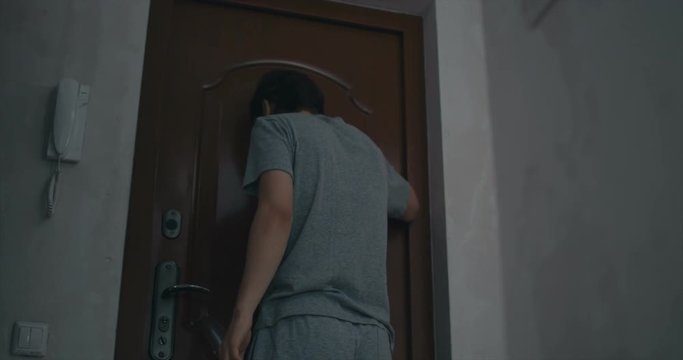 young man puts the bag behind the door and quickly closes the door, nervous