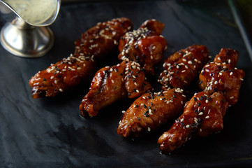 Baked chicken wings with sesame seeds and sweet sauce on a black square plate. close-up