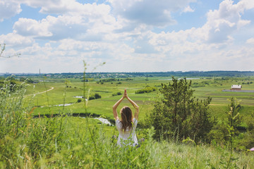 Young girl is doing yoga in the nature outdoors. Woman is practising asana on the hill in...
