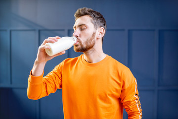 Conceptual portrait of a sports man in bright sweater drinking milk from the bottle on the blue...