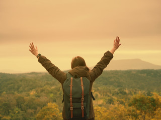 solo backpack and camping concept from backside of long hair woman in warm cloth with her bag travel, relax, happy  and see to forest and mountain in morning after sunrise