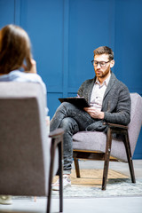 Handsome male psychologist listening to the woman client sitting during psychological session in the blue office interior