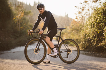 Professional road bicycle racer posing. Men cycling mountain road bike at sunset.