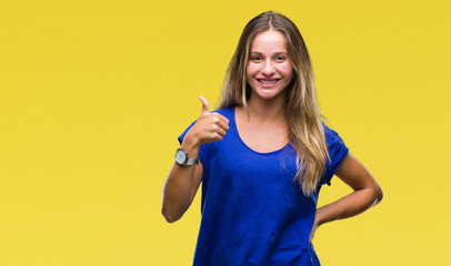 Young beautiful blonde woman over isolated background doing happy thumbs up gesture with hand. Approving expression looking at the camera with showing success.