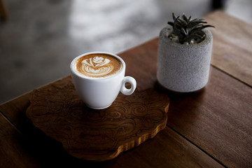 One cup of cappuccino with cactus in gray pot on wooden background.