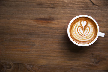 One cup of cappuccino with beautiful latte art on wooden brown background.