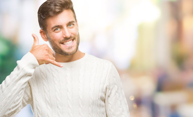 Fototapeta premium Young handsome man wearing winter sweater over isolated background smiling doing phone gesture with hand and fingers like talking on the telephone. Communicating concepts.