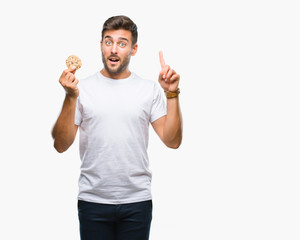 Fototapeta premium Young handsome man eating chocolate chips cookie over isolated background surprised with an idea or question pointing finger with happy face, number one