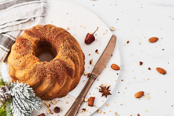 Vanilla and chocolate marble bundt cake surrounded by cinnamon, anise, hazelnut, dried orange crumbs on marble serving plate over white marble table. Top view with copy space for text.