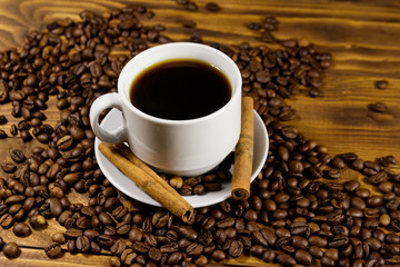 Cup of coffee, roasted coffee beans and cinnamon sticks on wooden table