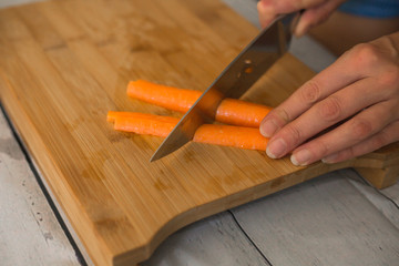 Woman with knife cutting carrot on wooden cutting board, close-up