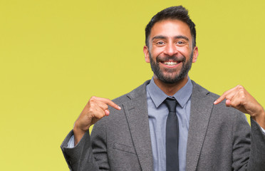 Adult hispanic business man over isolated background looking confident with smile on face, pointing...