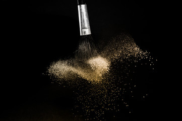 gold powder splash and brush for makeup artist or graphic design in black background, look like a luxury mood