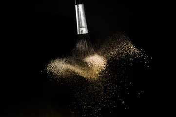 gold powder splash and brush for makeup artist or graphic design in black background, look like a...