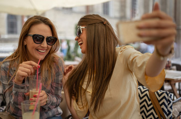 Two joyful attractive women taking a selfie while sitting together at cafe.