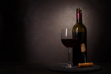 Fototapeta premium Wine bottle, glass with red wine and cork with corkscrew on dark wooden background. Celebration concept. Copy space
