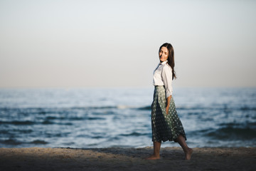 Marine female portrait. Attractive woman in green skirt walks along the shore before the sea