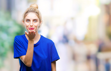 Young beautiful blonde and blue eyes woman wearing blue t-shirt over isolated background looking at the camera blowing a kiss with hand on air being lovely and sexy. Love expression.