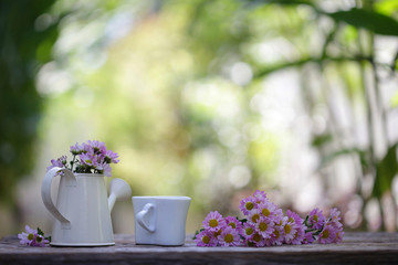 Pink Zinnia flower in water pot with cup on wooden table