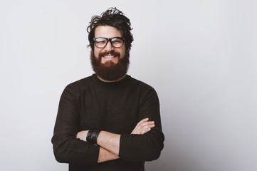 Happy smart handsome young man wearing glasses and smiling at camera crossing arms on white background.