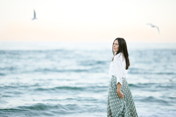 Marine female portrait. Attractive woman in green skirt walks along the shore before the sea while gulls fly over her