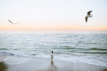 Marine female portrait. Attractive woman in green skirt walks along the shore before the sea while gulls fly over her