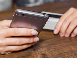 Close-up woman's hands holding a credit card and using smartphone for online shopping